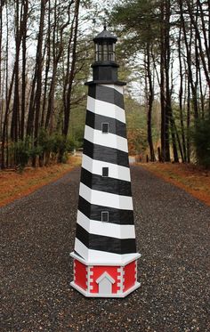 a black and white lighthouse sitting on the side of a road in front of trees