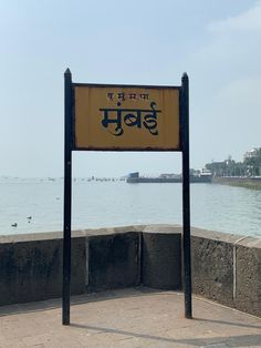 a yellow sign sitting on top of a cement wall near the ocean