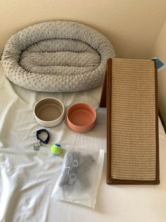 the cat bed is next to two bowls and other items