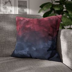 a red and blue pillow sitting on top of a couch next to a green plant