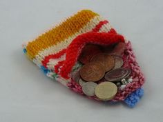 a small knitted purse with coins in it on a white surface, next to a penny