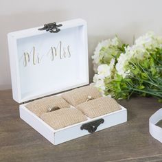 a white box with two rings inside sitting on a table next to flowers and a ribbon