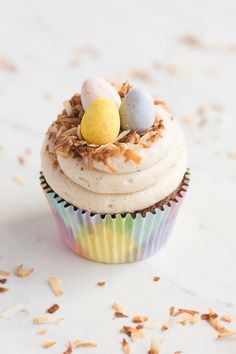 a cupcake with white frosting topped with an egg and sprinkles