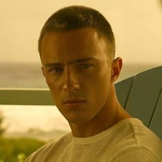 a young man sitting on a chair looking at the camera while wearing a white t - shirt