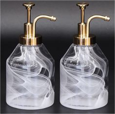 two glass soap dispensers with gold faucets