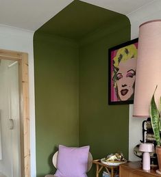 a living room with green walls and a pink lamp on the table next to a chair