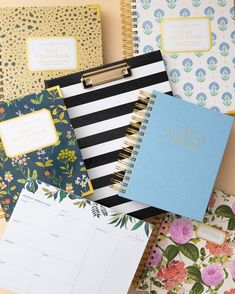 several notebooks and calendars are lined up on a table with colorful flowers in the background