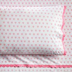 a bed with pink hearts and scalloped edges on the pillow case, along with two pillows