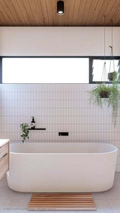 a white bath tub sitting under a window next to a wooden table and sink in a bathroom