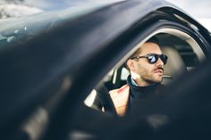 a man in sunglasses is looking out the window of a car while wearing his vest