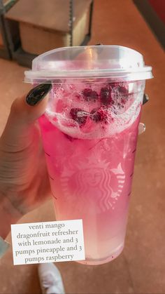 a person holding up a pink drink with ice and berries on it in a plastic cup