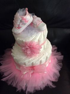 a pink and white diaper cake with baby shoes on it's bottom tier