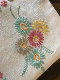 an embroidered piece of cloth with flowers and leaves on the side, sitting on a table