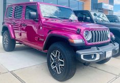 a bright pink jeep is parked in front of a building with other cars behind it