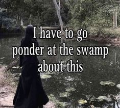 a person in a black robe standing next to a pond with lily pads on it