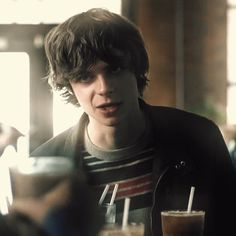 a young man sitting at a table with a drink in his hand and looking surprised