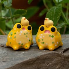 two yellow frog figurines sitting on top of a rock