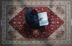 a man sitting on top of a rug with a laptop computer in his lap and looking at the screen