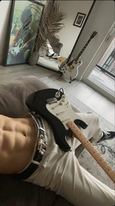 a man laying on top of a couch with a guitar in his lap next to him