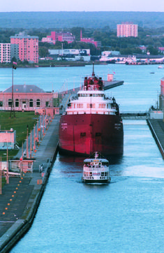 a large red boat traveling down a river next to a dock with buildings in the background