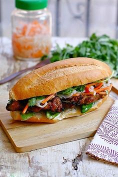 a sandwich with meat, lettuce and carrots sitting on a cutting board