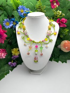 a necklace is displayed on a white mannequin next to colorful flowers and leaves