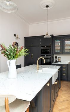 a kitchen with black cabinets and marble counter tops, gold handles and brass pulls on the faucet