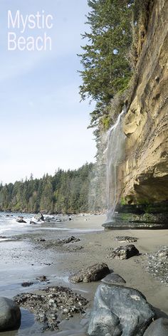 there is a waterfall coming out of the side of a cliff into the water and rocks on the beach