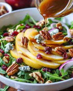 a salad with apples, pecans and cranberries is being drizzled with dressing