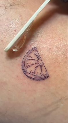 a small tattoo on the back of a woman's shoulder shows a slice of orange