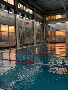 an indoor swimming pool with no people in it at sunset or dawn, near large windows