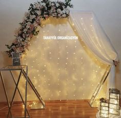 a white wedding arch with flowers and fairy lights on the wall in front of it