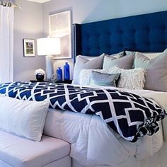 a bedroom with white and blue bedding, pillows and blankets on the headboard