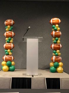 a man standing at a podium in front of two tall balloons with footballs on them