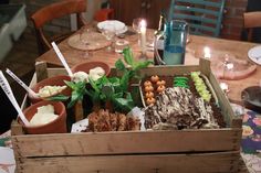 a wooden box filled with lots of food on top of a table next to candles