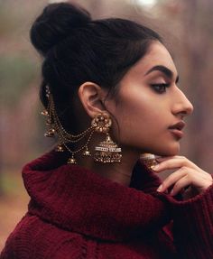 a woman with dark hair wearing gold earrings and a red sweater looking off to the side