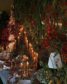 a table topped with lots of food next to candles and trees filled with flowers in the background