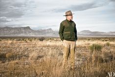 a man standing in the middle of an open field with mountains in the back ground