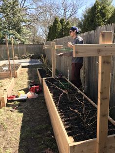 a man standing next to a wooden raised garden bed filled with dirt and shrubbery