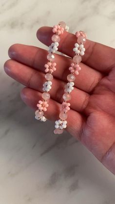 a hand holding some pink and white flowers on it's fingers with the beading off