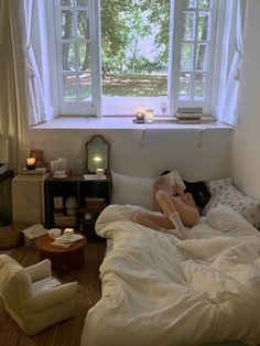 a woman laying in bed with her feet up on the pillow next to an open window