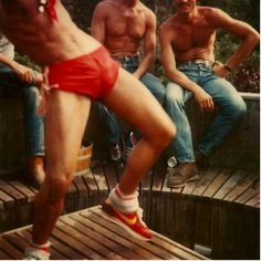 a woman in red shorts is dancing on a wooden deck with other people sitting around her