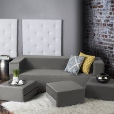 a living room with grey couches and white rugs on the floor in front of a brick wall