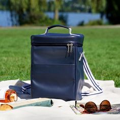 a blue bag sitting on top of a blanket next to sunglasses and an umbrella in the grass