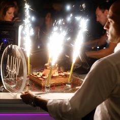 a cake with lit candles on it sitting in front of some people