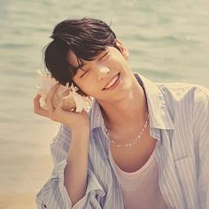 a young man is sitting on the beach and holding a seashell in his hand