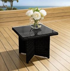 a vase with white flowers sitting on top of a glass table next to the ocean