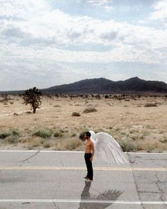 a man standing in the middle of an empty road with his wedding veil blowing in the wind