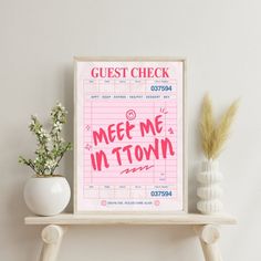 a pink poster with the words meet me in town on it next to a vase