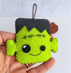 a hand holding a green and black felt ornament with a creepy face on it